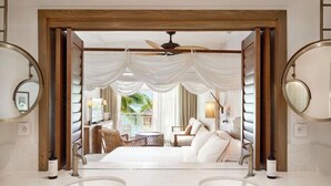 Une chambre luxueuse dotée d’un grand lit, de deux miroirs ronds, d’un ventilateur de plafond et offrant une vue sur un balcon aménagé avec des sièges d’extérieur.