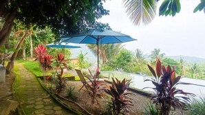 Un sendero de jardín con un patrón de baldosas hexagonales, rodeado de diversas plantas y un paraguas azul.