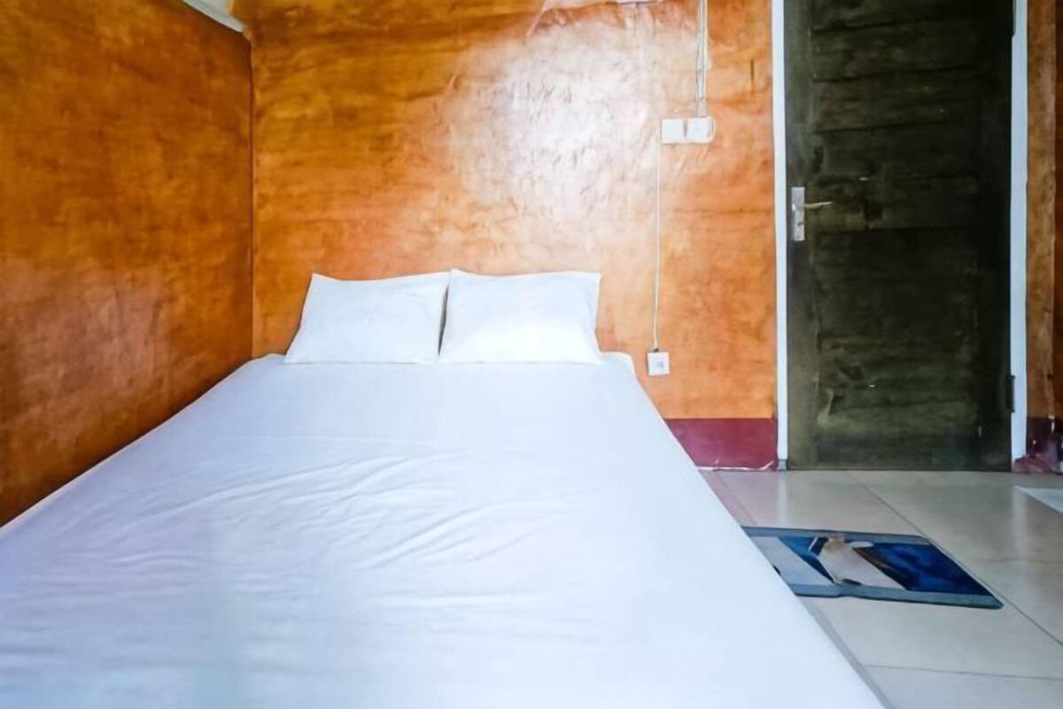 A room with a bed, wooden walls, a door, and a floor mat.