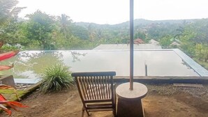 Un patio con una silla y mesa de madera, con vista a una piscina y abundante vegetación.