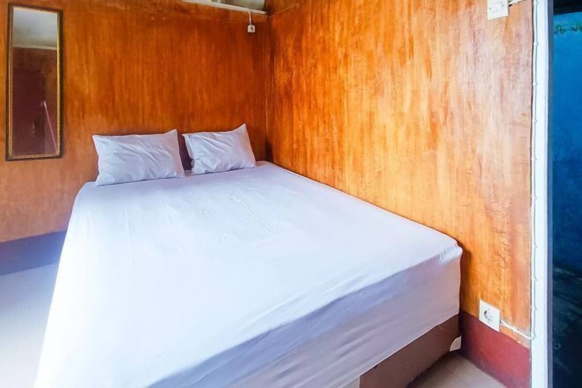 A single-bed room with wooden walls, a white bedspread, and a mirror on the left wall.