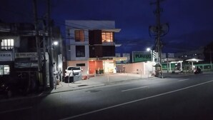 A street view at dusk with a modern building, a gas station, and a parked car. - 8 ZHENSEN INN (Bacoor)