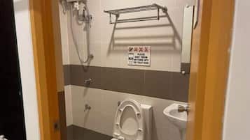 A small bathroom with a toilet, a sink, and a shower. There is a sign on the wall that says "Please don't throw anything into the toilet bowl."
