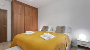 A bedroom with a bed, wooden wardrobe, bedside table with a lamp, and a bench. - Premium Downtown Queen Apartment KARTULI (Reykjavík)