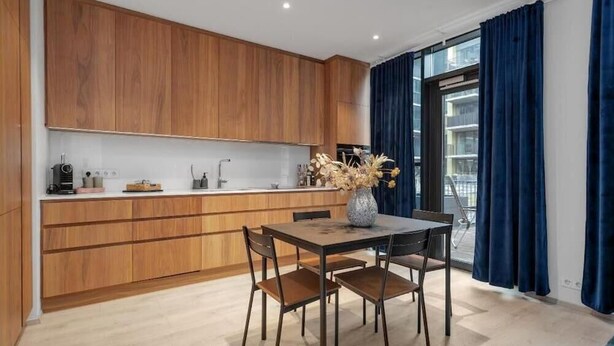 A modern kitchen with wooden cabinets, a dining table with chairs, and a vase with dried flowers. - Premium Downtown Queen Apartment KARTULI (Reykjavík)