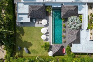 Vista aérea de una casa moderna con piscina, mobiliario exterior y exuberante jardinería.