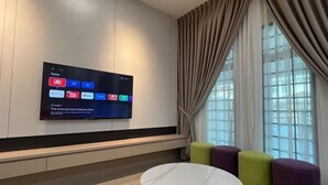A modern hotel lobby with a flat-screen TV displaying various streaming services, a round marble table, and colorful ottomans. - 5 min to AeonBig , Old Street, BP Mall & D Garden (Simpang Kanan)