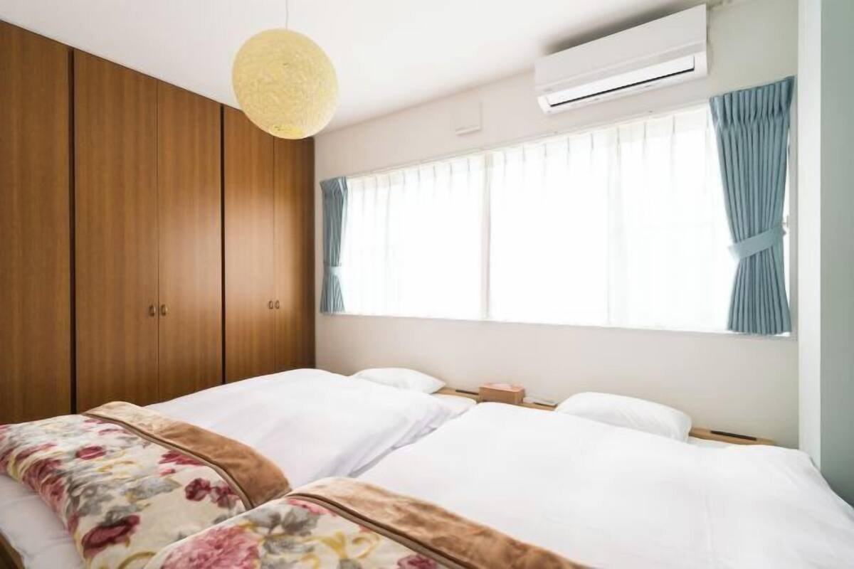 Een slaapkamer met twee bedden, een houten garderobe, een airconditioning en een raam met gordijnen.