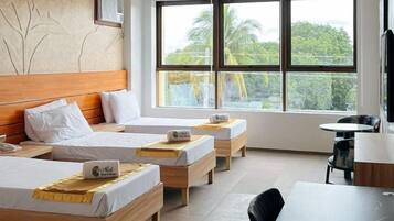 Habitación de hotel con dos camas, cabecero de madera, una mesita, una silla y ventana con vistas a zonas verdes.