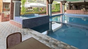 A swimming pool with a tiled deck, a seating area, and a view of a hotel in the background. - RedDoorz Plus @ Nick Hotel Guimba (Guimba)