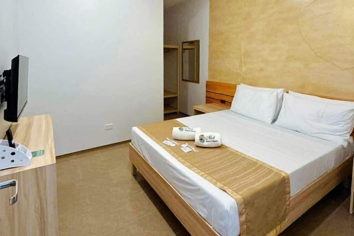 A hotel room with a bed, a desk with a computer, and a mirror.