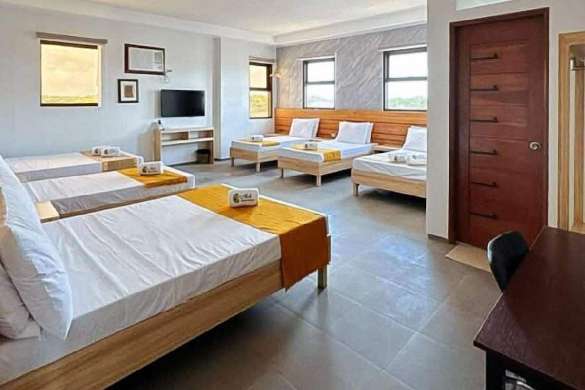 A hotel room with three single beds, a TV, a desk, and a wooden door.