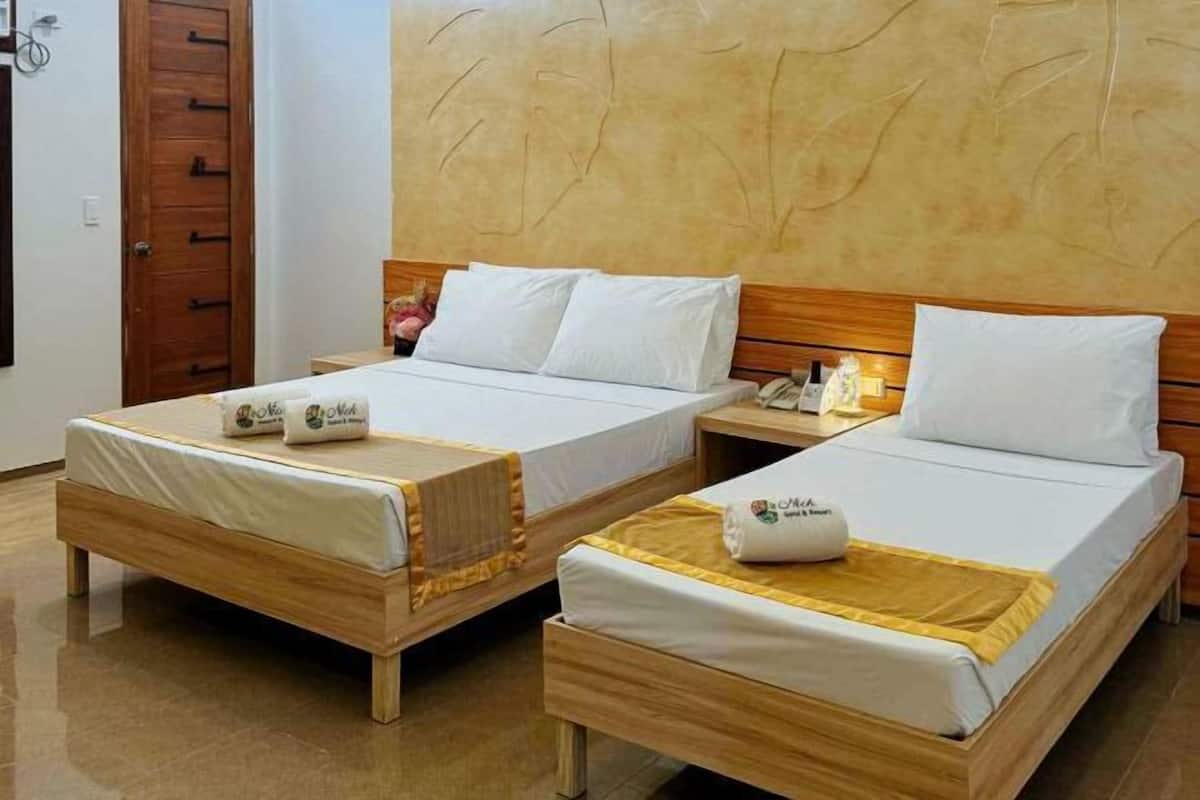 Two wooden beds with white bedding and a wooden headboard, a wooden nightstand with a lamp, and a wooden door.