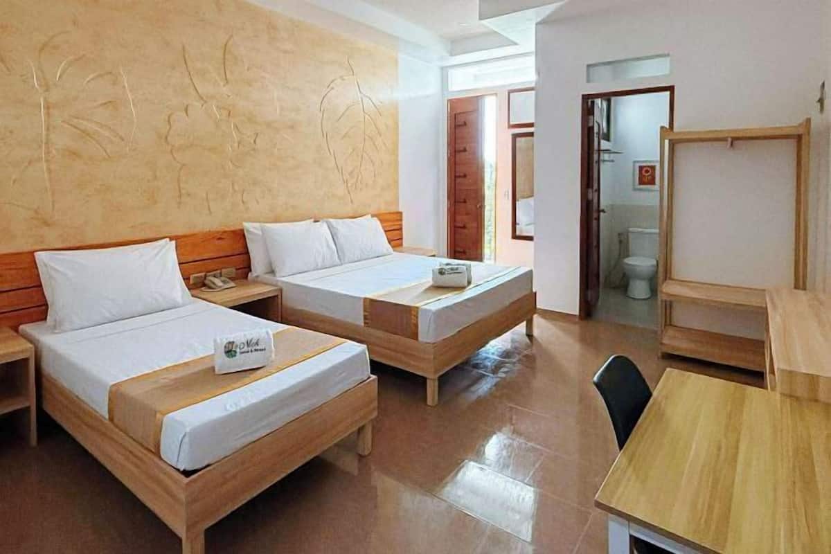 A hotel room with two wooden beds, a wooden desk, and a bathroom visible through an open door.