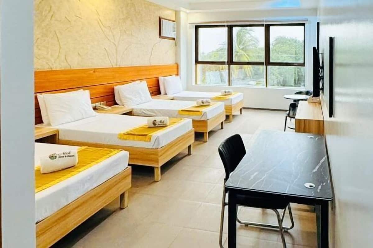 A hotel room with three wooden beds, a desk, and a chair.
