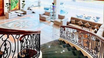 A hotel lobby with a staircase, seating area, and a view of the street.