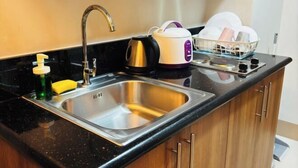 A kitchen with a stainless steel sink, a kettle, a dish rack, and a bottle of dish soap. - Solana Staycation Suites at Shore 3 Residence (Pasay)
