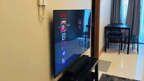 A flat-screen TV mounted on a wall, a telephone, and a dining area with a table and chairs. - Solana Staycation Suites at Shore 3 Residence (Pasay)
