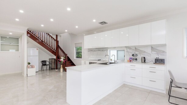 Une cuisine moderne avec des meubles blancs, un îlot central et un escalier en bois.