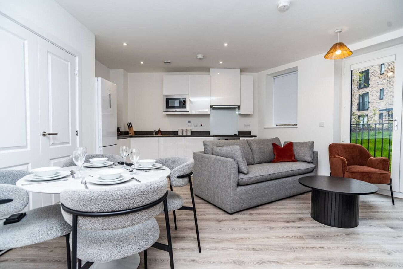 A modern living room with a grey sofa, a round dining table set for four, and a small coffee table.