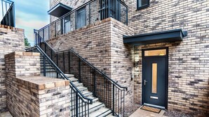A modern building with a brick exterior, a black door, and a staircase with black railings. - Belgrave Village | Central Apartment (Balsall Heath)