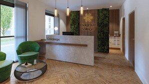 A reception area with a modern design, including a reception desk labeled "Concierge" and "Belgrave Village," a green upholstered chair, a round coffee table, and a herringbone wooden floor. - Belgrave Village | Central Apartment (Balsall Heath)