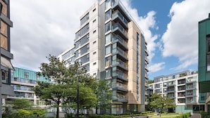 Um edifício residencial moderno, com várias andares e varandas, rodeado por vegetação e um céu claro.
