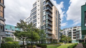 Un moderno grattacielo con numerosi balconi, circondato dal verde e da altri edifici residenziali.