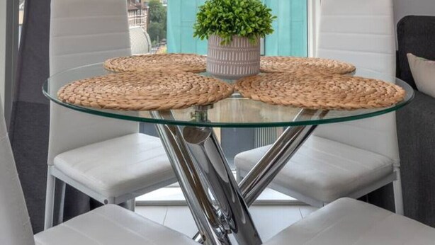 A modern dining area with a glass table, white chairs, and a view of the cityscape through large windows. - Clerkenwell Flat: Pet-Friendly, Balcony Views (Greater London)