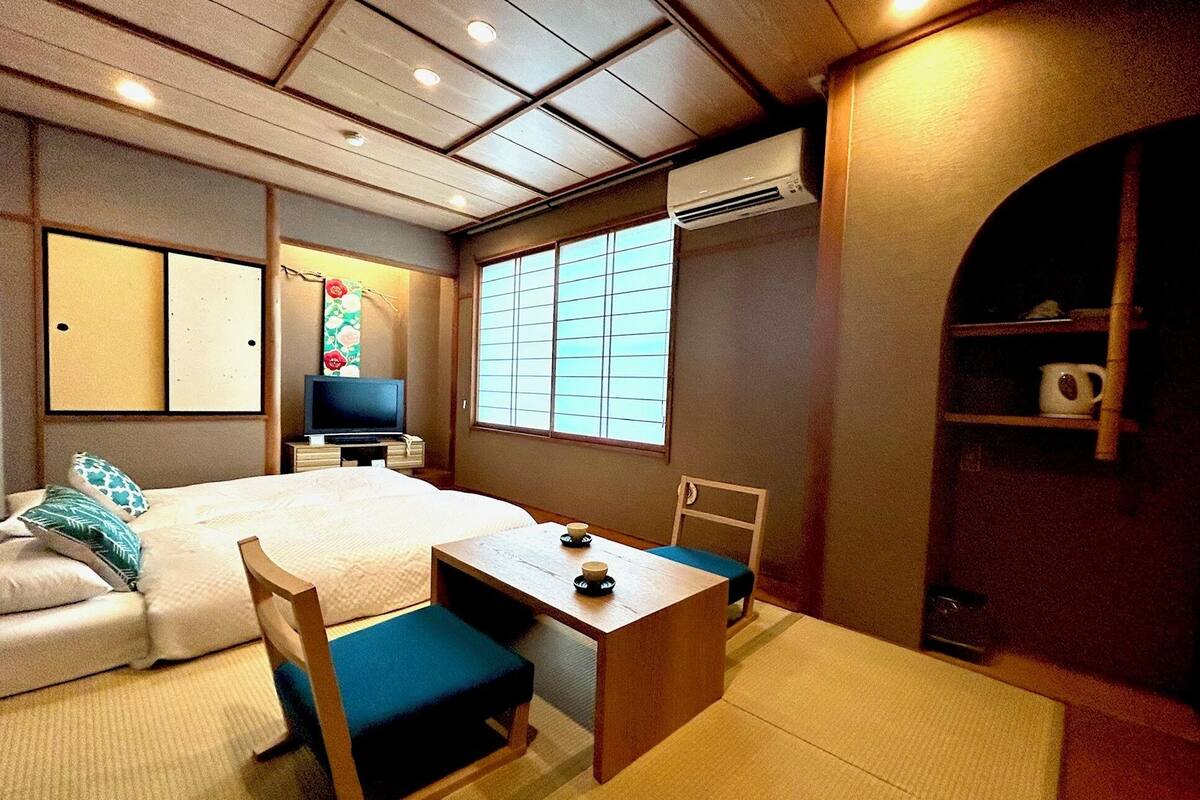 A traditional Japanese-style room with tatami flooring, a bed, a television, and a window with shoji screens.