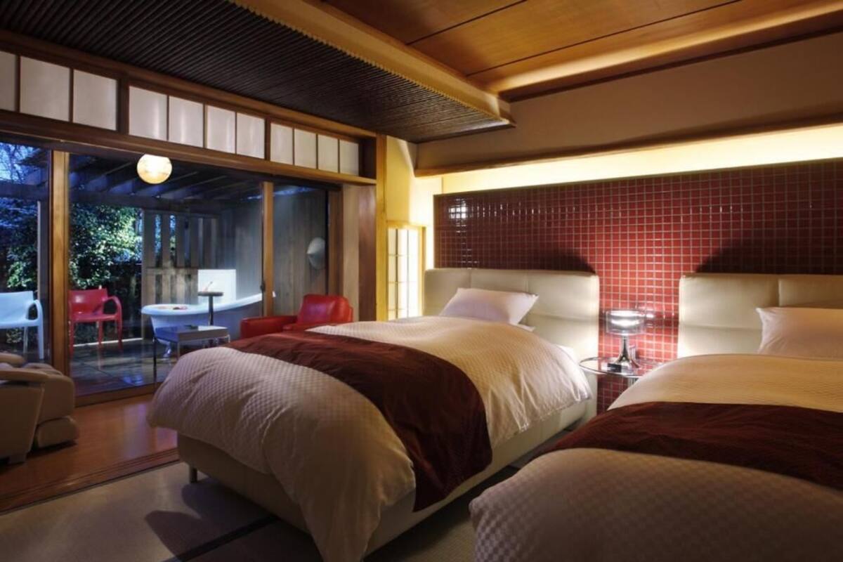A hotel room with two beds, a sliding glass door leading to an outdoor area, and a red-tiled wall.