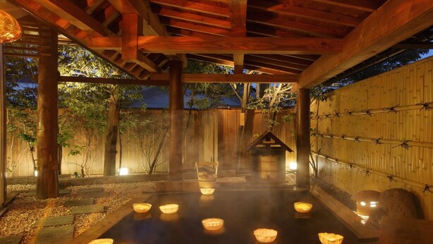 A traditional Japanese onsen with a wooden structure, a stone bath, and multiple lit candles. - Hanaakarinoyado Tsukinoike (Kaminoyama)
