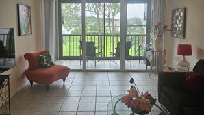 Ein Wohnzimmer mit einem roten Sofa, einem Glastisch und einem Balkon mit Gartenmöbeln.