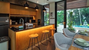 Une cuisine moderne avec des meubles en bois, un îlot central doté de tabourets et une vue sur une piscine.