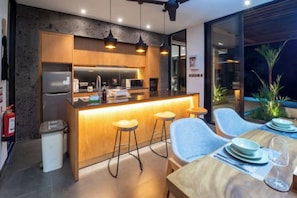 A modern kitchen with a central island, bar stools, and a dining area with a table and chairs. - Villa Purnama Ubud by BaliSuperHost (Bali)