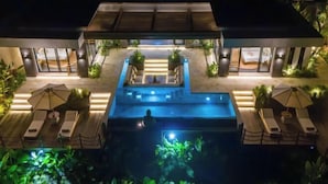 Un espace piscine aménagé sur le toit, avec des chaises longues et des parasols, entouré de plantes et doté d’une passerelle couverte.