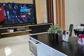 A modern living room with a flat-screen TV displaying streaming services, a coffee maker, and a plant on a wooden table. - The Elements @ Ampang (Kuala Lumpur)