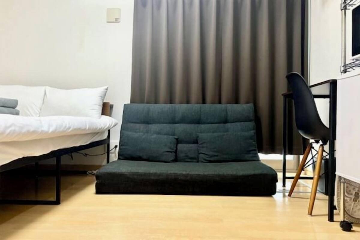 Een kamer met een bed, een donkergroene bank, een zwarte stoel en een gordijn.