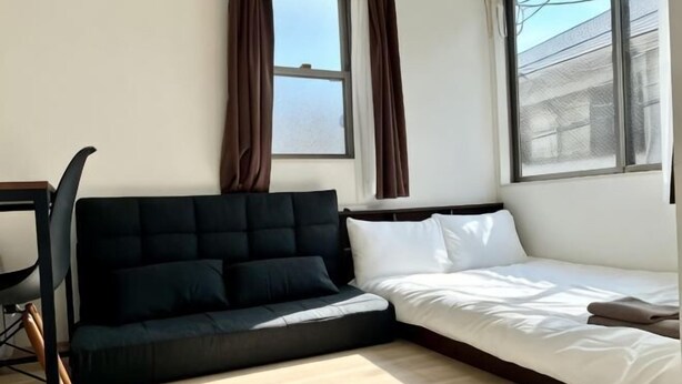 A room with a black sofa, a white bed, and a window with curtains.