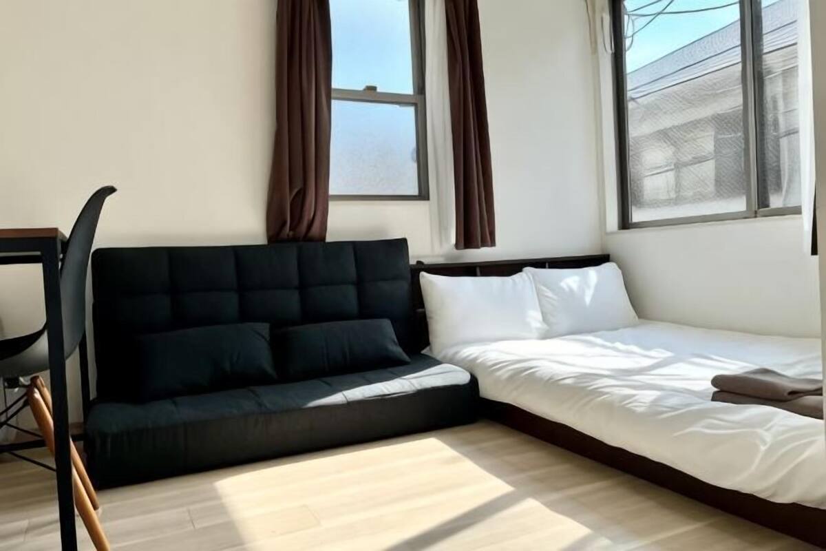 Een kamer met een zwarte bank, een wit bed en een raam met gordijnen.