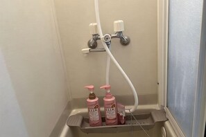 A bathroom with a shower, a sink, and two bottles of lotion on a shelf.
