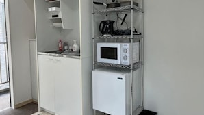 A compact kitchenette with a microwave, coffee maker, and storage shelves.