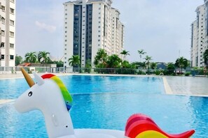 A swimming pool with a unicorn float, surrounded by tall residential buildings and palm trees. - Beautiful Suria Kipark Damansara 3R2B Apartment (Batu)