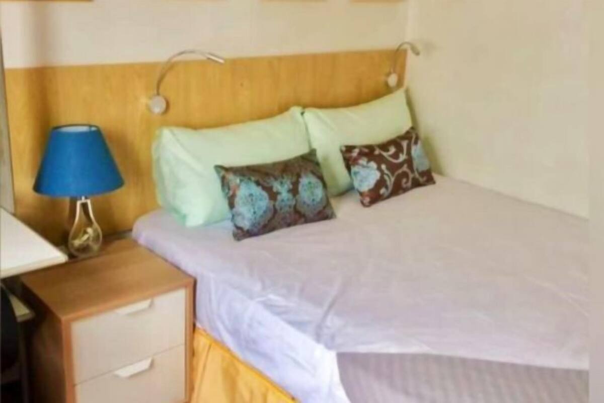 A bed with a headboard, a bedside table with drawers, and a lamp.