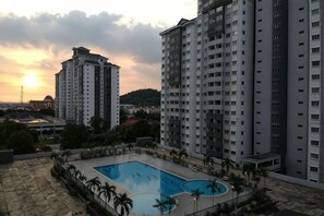 Ein Wohngebäude mit Pool auf dem Dach, umgeben von Hochhäusern, mit Sonnenuntergang im Hintergrund.