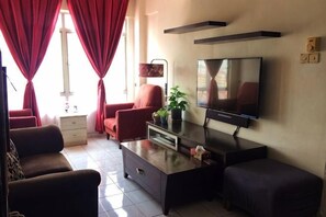 Una sala de estar con sofá, sillón, mesa de centro, televisor y planta en maceta.