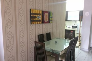 A dining area with a glass table and chairs, a kitchen in the background, and patterned wallpaper. - Beautiful Suria Kipark Damansara 3R2B Apartment (Batu)