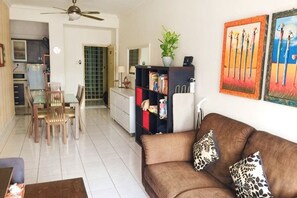 A living room with a brown sofa, a dining area with chairs, a kitchen, and a ceiling fan. - Beautiful Suria Kipark Damansara 3R2B Apartment (Batu)