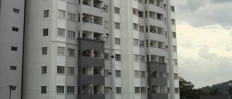 Um edifício residencial com vários andares, varandas, piscina e área cercada.
