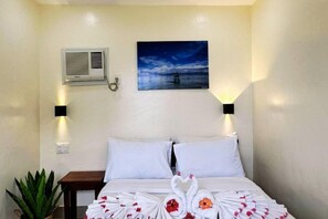 Een hotelkamer met een bed, twee wandlampen, een airconditioning en een schilderij van een strandgezicht.